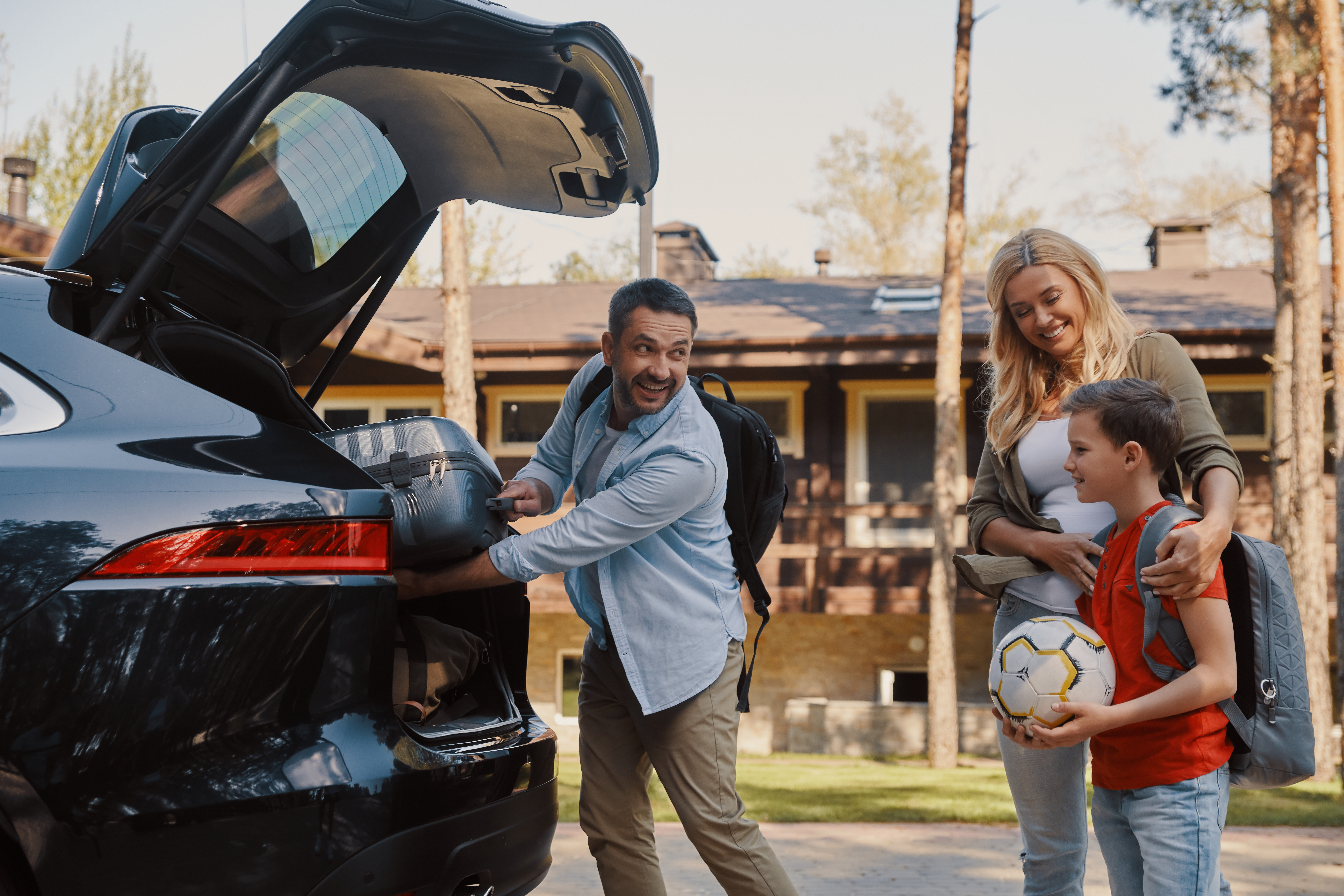 Man, woman and child behind car, loading the trunk with kid's soccer equipment.