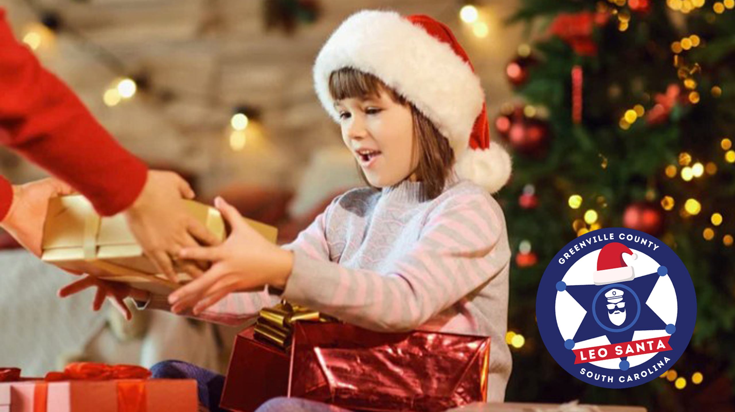 Young child receives a gift image includes the Greenville County Leo Santa logo.